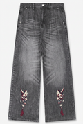 Wide-leg gray denim jeans with embroidered devil mask motifs on the lower left and right legs, shown flat against a light gray background.