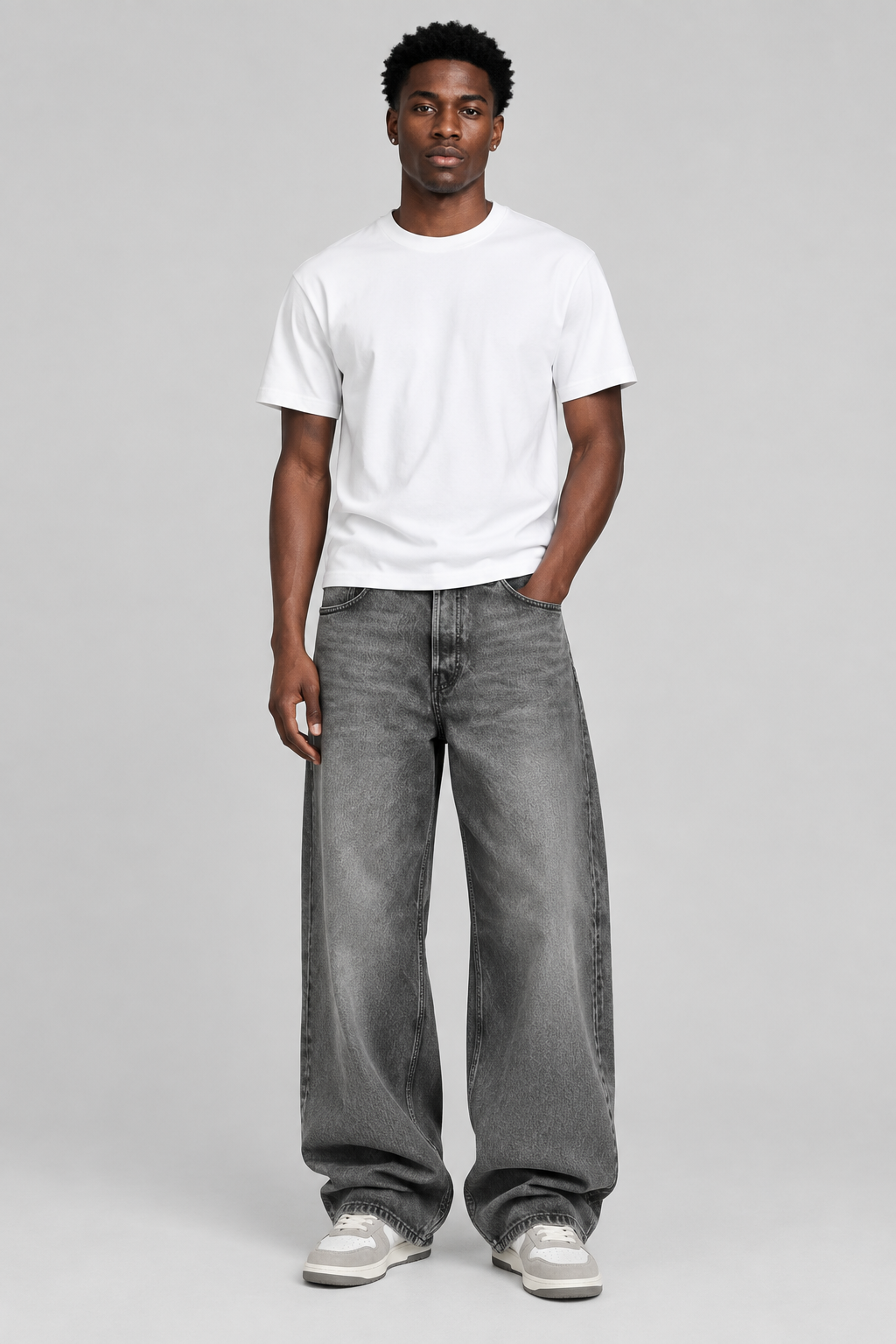 A man modeling a white crew-neck t-shirt and wide-leg gray denim jeans, standing against a solid light gray studio background.