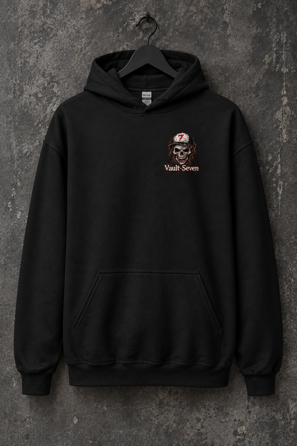 A black pullover hoodie hanging on a black hanger against a textured dark gray wall. The hoodie features a small chest graphic of a skull wearing a hard hat with a red '7' and the text 'Vault Seven' printed below it.