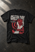 A black short-sleeve graphic t-shirt featuring the Green Day 'American Idiot' album artwork, laid flat on a dark textured concrete surface.