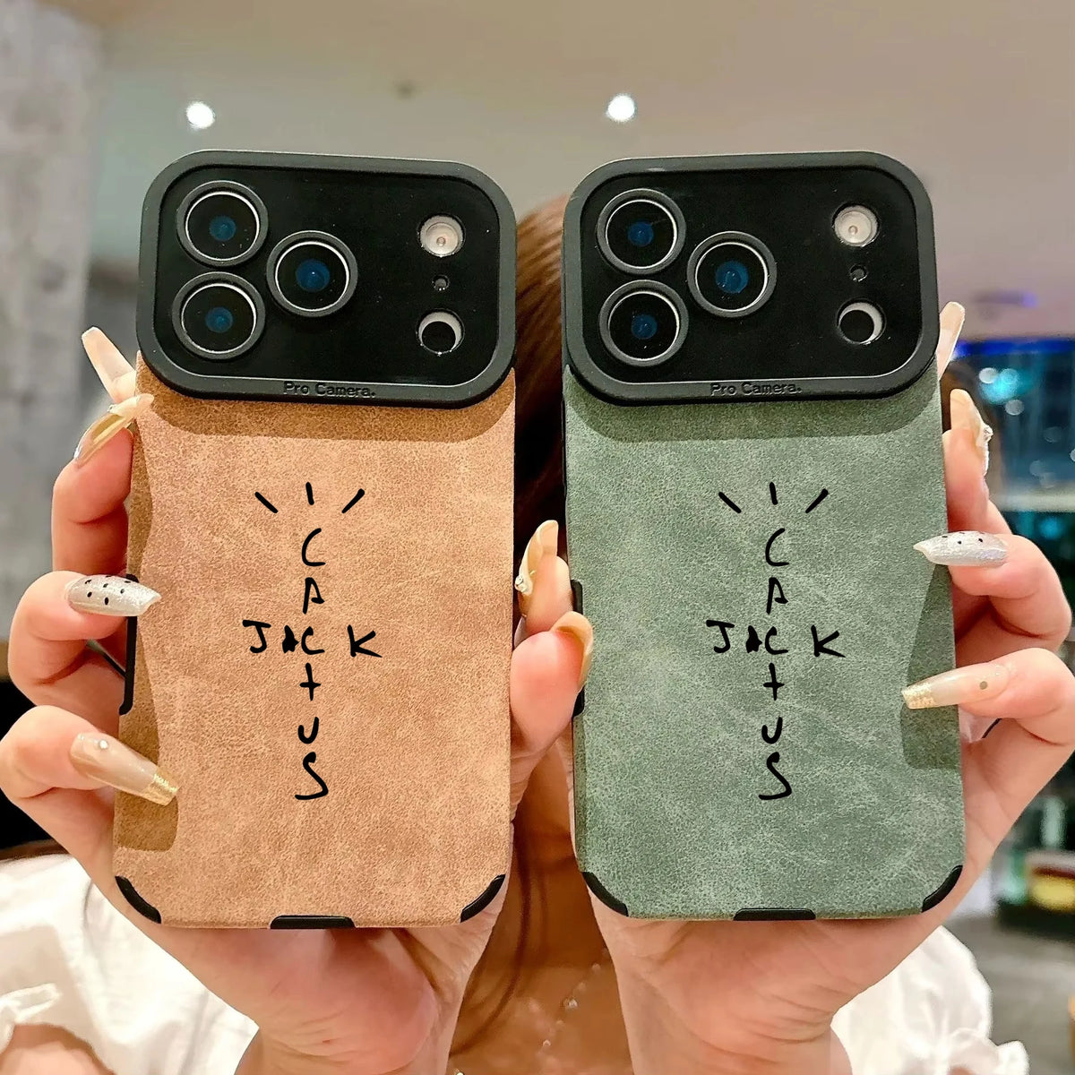 Two phone cases held up by hands, one in tan and one in sage green, both with a black camera bar and the word 'Cactus Jack' printed in black on the back.