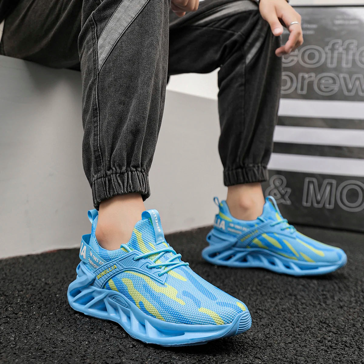 A person wearing light blue athletic sneakers with yellow flame-like accents, paired with dark gray jogger pants, seated on a white block with a black-and-white sign in the background.