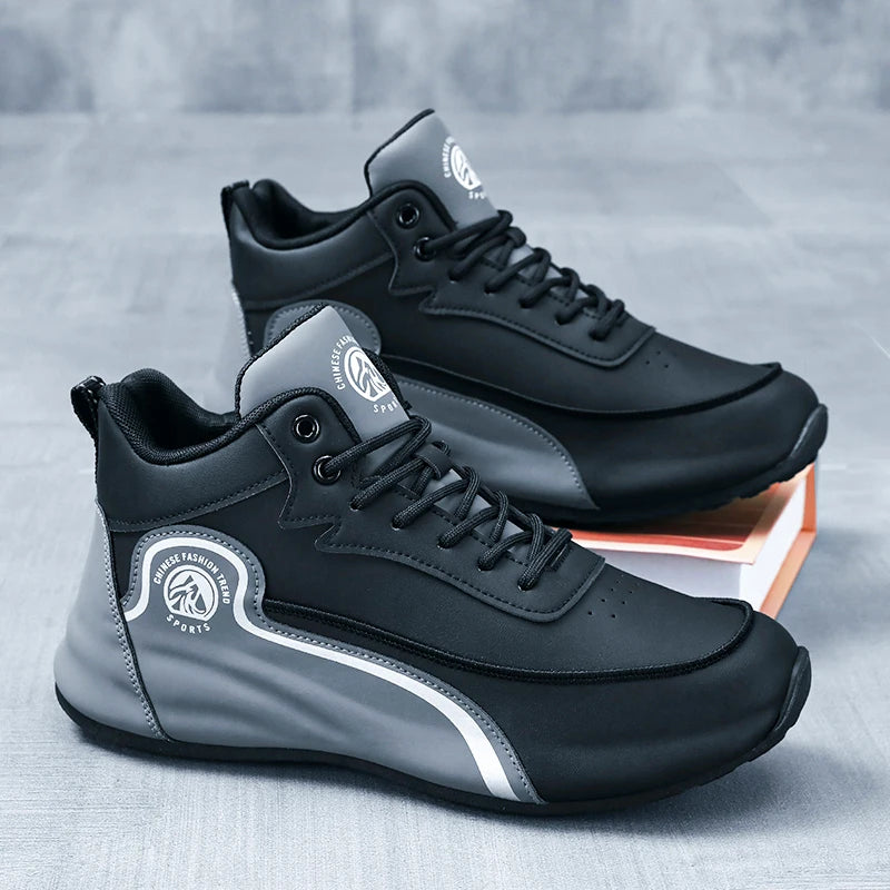 A pair of black and gray athletic sneakers with white accents, displayed on a textured gray surface with one shoe resting on an orange book.