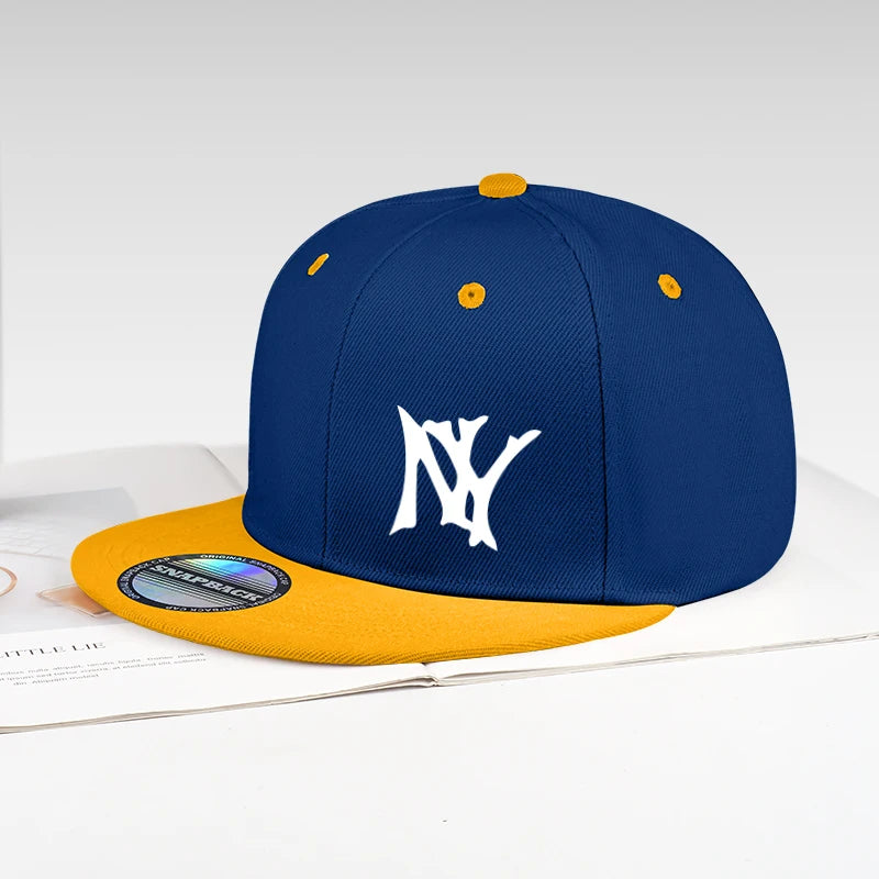 A structured snapback cap with a navy blue crown, a mustard yellow flat brim, and a white embroidered 'NY' logo on the front. The cap is styled on top of an open book against a clean white background.