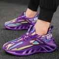 A close-up of a person wearing purple mesh sneakers with yellow and light blue abstract stripes, standing on a dark asphalt surface. The shoes feature a chunky sculpted purple sole and the brand name 'BENELLIA' printed on the side.