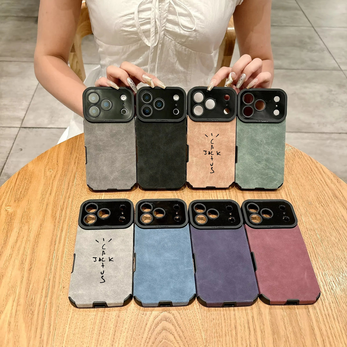 Person holding eight different phone case options on a wooden table.