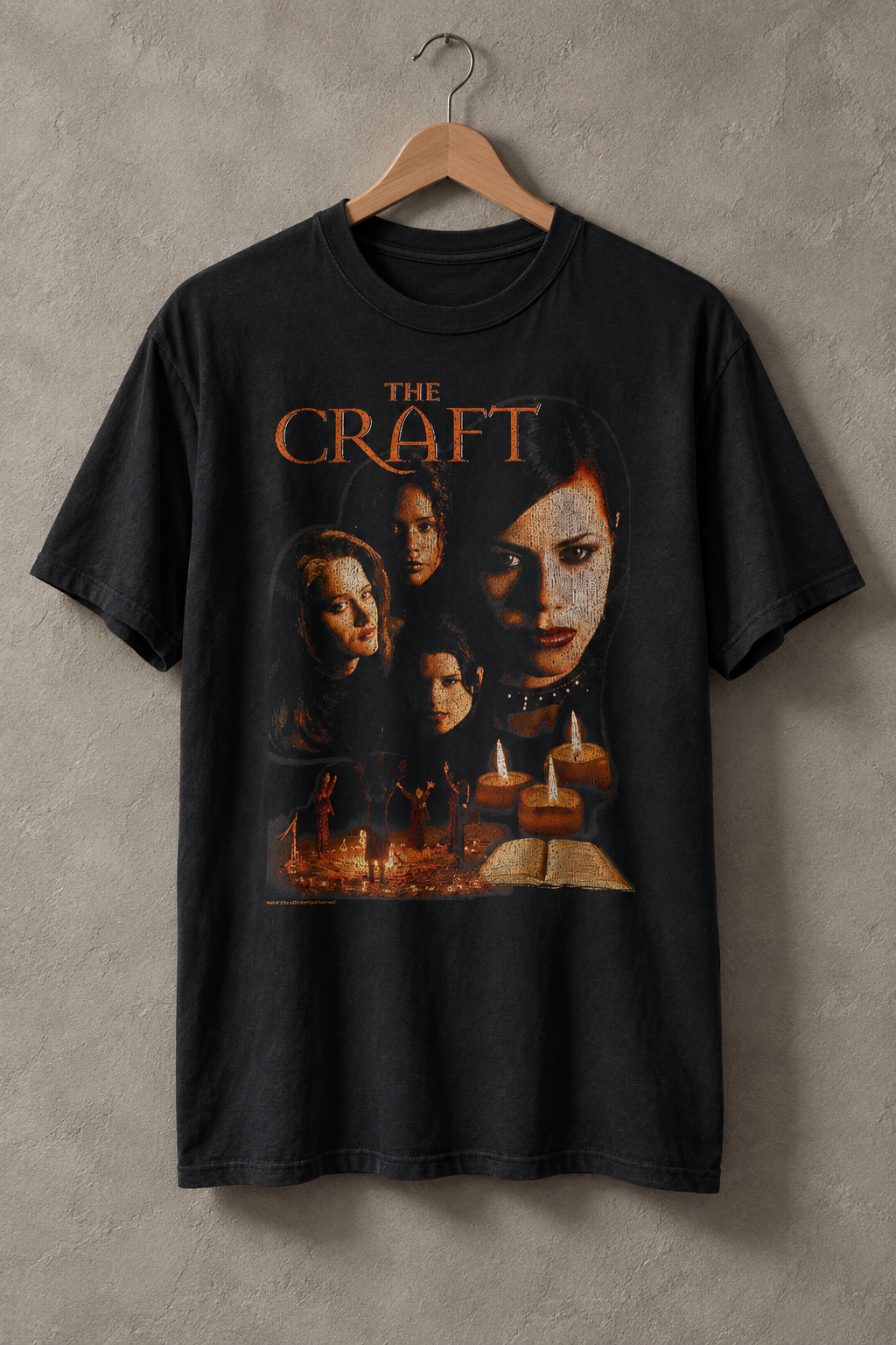 A black graphic t-shirt featuring characters and the title 'The Craft' in orange, hanging on a wooden hanger against a textured gray wall.