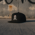 Vault-Seven black flatbill snapback on a gritty West Coast streetwear background